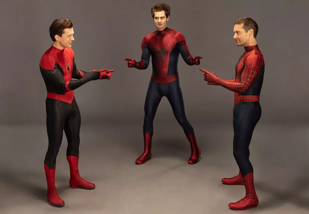 Tobey Maguire, James Garfield and Tom Holland in their Spider-Man suits point at each other.